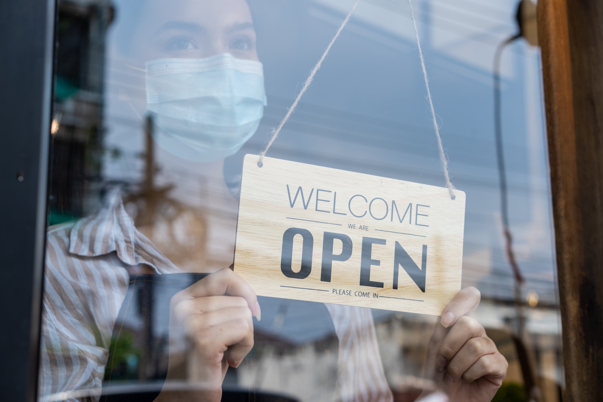Caucasian Coffee shop owner wear mask due to Covid19, turns Welcome open sign on door to reopen.